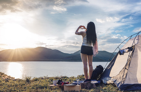 young woman make hands in heart shape show up to the sky and enjoy view of magnificent landscape while tenting on vacation.の写真素材