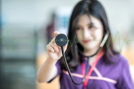 Beautiful young nurse holding stethoscope and  listening to green pulse and heart rates の写真素材