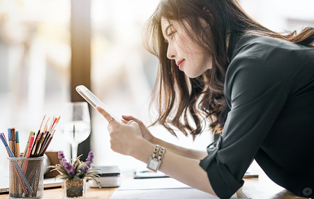 Rear view of beautiful female designer holding and looking at tablet screen while working at modern officeの写真素材