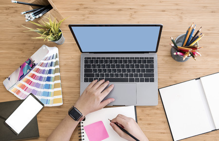 Top view of designer using laptop on desk at office with blank screen smartphone,graphic designer table montage.の写真素材
