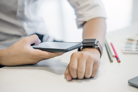 Businessman using smartphone connect to smartwatch while working at office.New technology conceptの写真素材