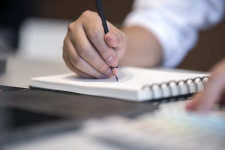 Close up view image of man writing on notebook while working at officeの写真素材