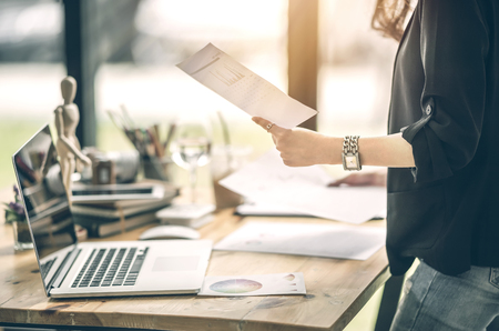 Cropped image of young businesswoman holding paperwork while standing near her desk at officeの写真素材