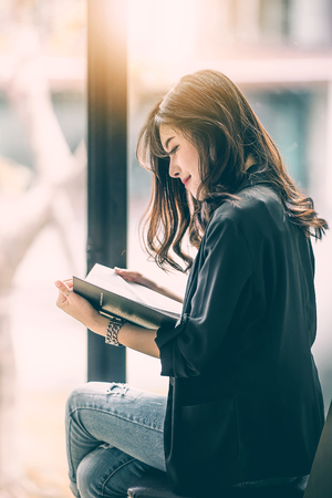 Beautiful woman reading a book by the window with morning sunlightの写真素材