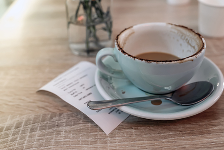 Dirty cup of coffee after drink with receipt slip on wooden tableの写真素材