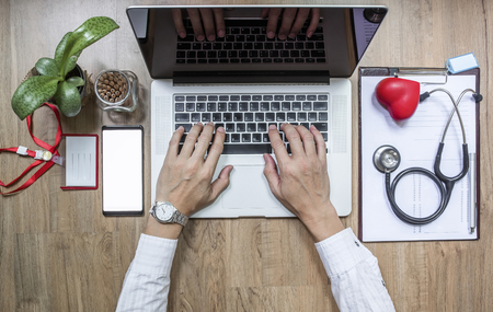 Doctor working at office desk and using a laptop computer, top viewの写真素材