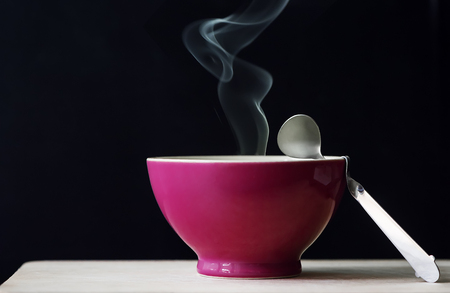 Red bowl of hot soup with smoke on black backgroundの写真素材