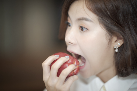 Close up shot of beautiful woman open wide mouth to bite the red apple.の写真素材