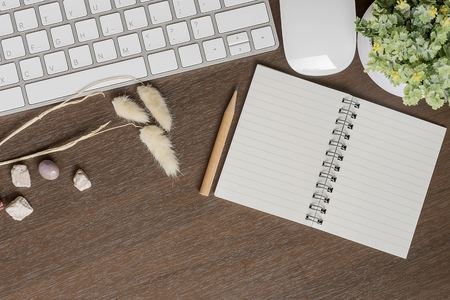 Top view of white keyboard, mouse, blank notebook, pencil and houseplant on wooden table with copy spaceの写真素材