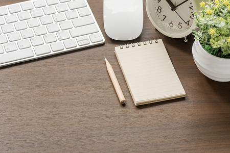 Mockup of white keyboard, mouse, blank notebook, pencil,alarm clock and houseplant on wooden table with copy spaceの写真素材