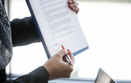 close up female hand holding pen pointing at document paper for sign contractの写真素材
