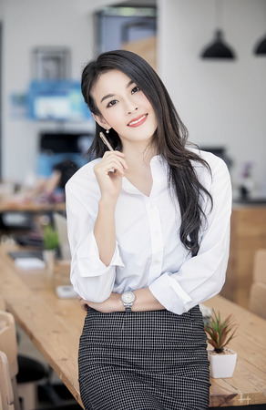 Portrait of successful middle aged businesswoman holding pen and standing at her office.の写真素材