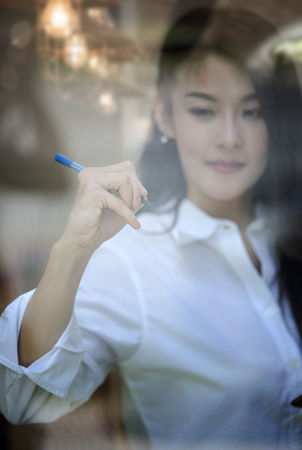 young Caucasian businesswoman writing or drawing something on blank glass board with pen markerの写真素材