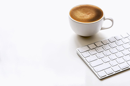 cup of coffee and white keyboard on white table with copy spaceの写真素材