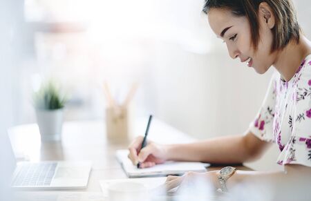 Beautiful professional businesswoman writing down her idea on notebook while working in the modern office with happiness.の写真素材