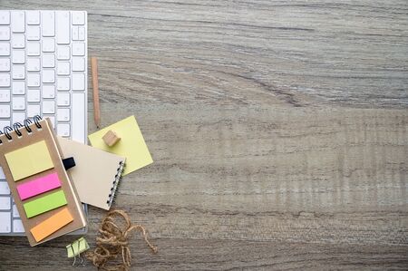 mockup white keyboard, notebook, pencil and sticky note on wooden table background, top view and copy space.の写真素材