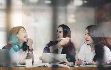 Women having fun while working together at cafe, laughing and enjoying while working. Looking through window glass.の写真素材