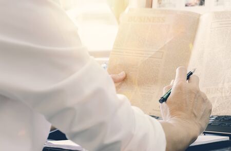 Cropped image businessman holding pen and reading newspaper while sitting at office desk.の写真素材