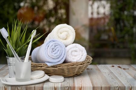 Clean towels in basket with toothbrush and houseplant on wooden table with green nature backgrouond.の写真素材