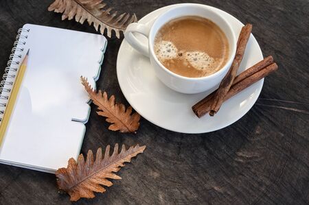 Top view cup of coffee with notebook and dry leaf on wooden background, copy space.の写真素材
