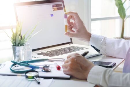 hand of doctor holding urine tube for test while working with laptop. Physician with urinalysis for test urea examination.の写真素材