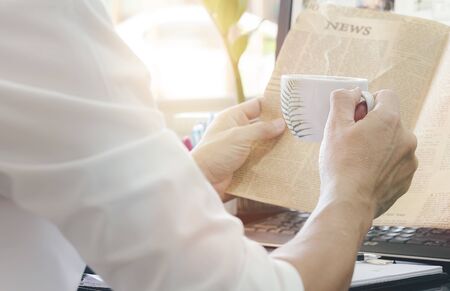 Cropped image of man with cup of coffee reading newspaper while take a break in modern office.