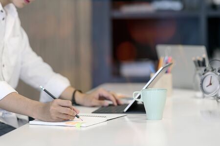 Cropped shot of man writing on notebook with pencil while sitting at office desk.の写真素材