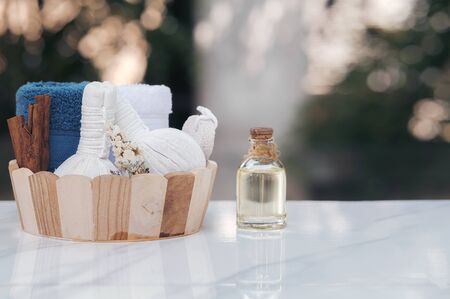 Spa treatments set in wooden bucket with herbal compressing ball, oil bottle, candles and towel on marble top table. Beauty and body care concept.の写真素材