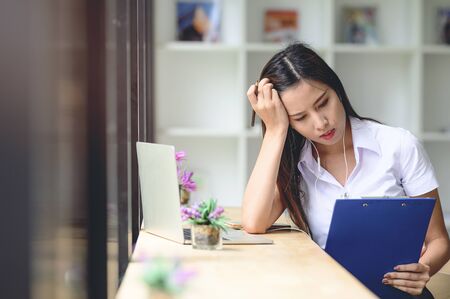 Worried and sad student female searching information in a laptop and looking at clipboard in her hand.の写真素材