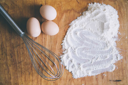 whisk, eggs and flour on wood board with space for text