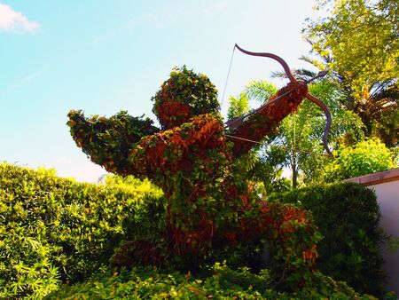 Cupid shaped topiary in garden surrounded by other plants and tropical botanicals の写真素材