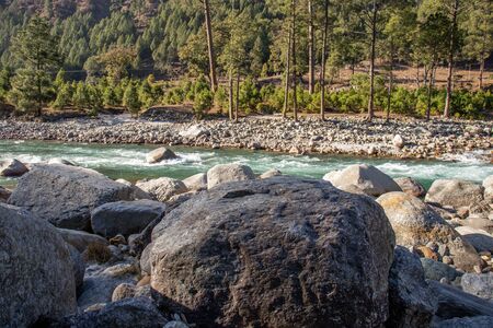 A small creek flowing through the valleys of the himalayan mountains with big rocks and pebblesの写真素材