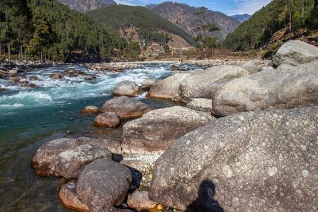 A small creek flowing through the valleys of the himalayan mountains with big rocks and pebblesの写真素材