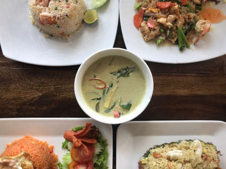 Top view of five type of Thai dishes served on a table. Seafood fried rice, seafood fried noodle, green curry soup, Tomyam fried rice and Thai seafood pineapple rice.の写真素材