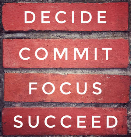 Motivational and inspirational quote - âDECIDE, COMMIT, FOCUS, SUCCEEDâ written on red brick wall. Vintage styled background.の写真素材