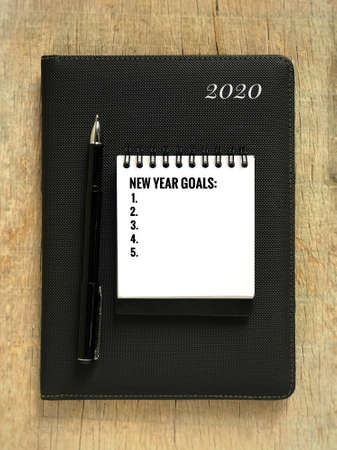 New Year resolutions concept - âNEW YEAR GOALSâ Written on a white notepad and placed on top of a 2020âs planner book.の写真素材