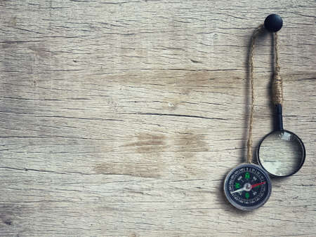 Conceptual - A navigation compass and magnifying glass hang against a wooden wall.の写真素材