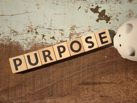 Motivational and inspirational word - PURPOSE written on wooden blocks and a piggy bank placed on a wooden table.の写真素材