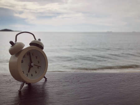 An alarm clock on a wooden table on background of a sea.