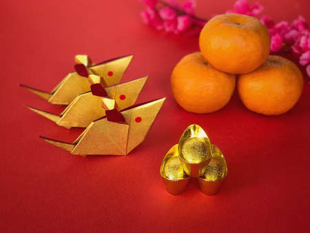 Chinese New Year concept. Golden origami rats, golden ingots, mandarin oranges and chinese cherry blossom flower on red background. The Chinese words written on the top of the ingots literally means âlucky fortuneâ.の写真素材