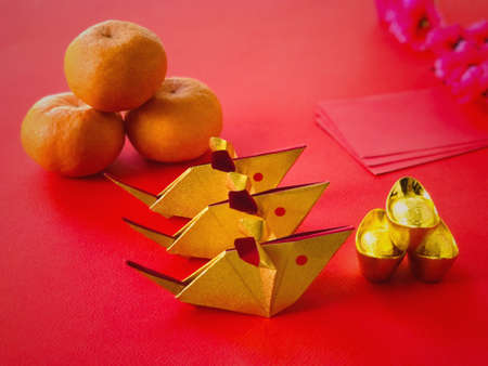 Chinese New Year concept. Golden origami rats, golden ingots, mandarin oranges, ang paos and chinese cherry blossom flower on red background. The Chinese words written on the top of the ingots literally means âlucky fortuneâ.の写真素材