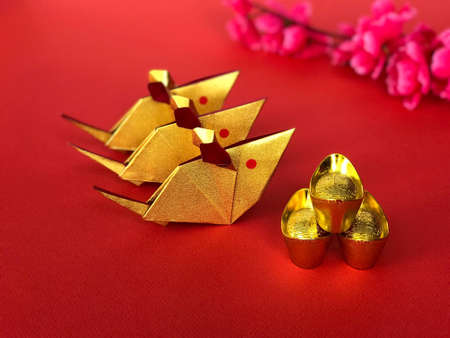 Chinese New Year concept. Golden origami rats, golden ingots, and chinese cheery blossom flower on red background. The Chinese words written on the top of the ingots literally means âlucky fortuneâ.の写真素材