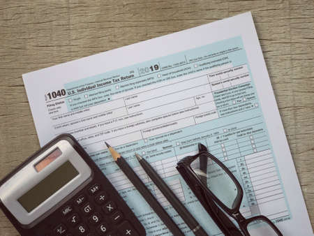 Tax-filling concept. A calculator, pencil, pen, eyeglasses and featuring half of U.S IRS 1040 form. With vintage-styled background.の写真素材