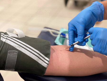 Close up of hands in blue gloves injecting a needle into a man left arm for the blood draw for...