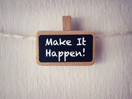 Motivational and inspirational wording. Make It Happen written on a wooden tag. With blurred styled background.の写真素材