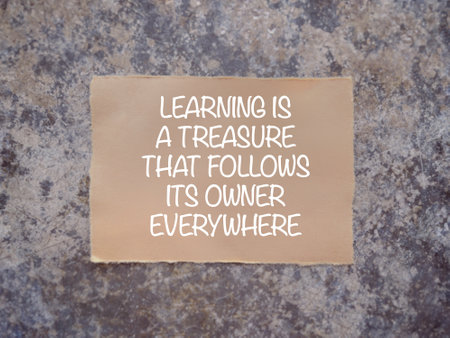 Motivational and inspirational wording. Learning concept. LEARNING IS A TREASURE THAT GOLLOWS ITS OWNER EVERYW written on a paper. With blurred styled background.の写真素材