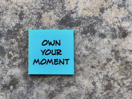 Motivational and inspirational wording. OWN YOUR MOMENT written on a notepad. With blurred styled background.の写真素材