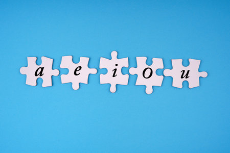 Communication, learning and education concept. The vowels aeiou written on jigsaw puzzle pieces. With light blue background.の写真素材