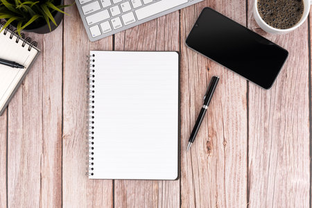 Flat lay view of a laptop, notebooks, a pen and a mobile phone, on a wooden tableの写真素材