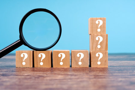 Question Marks On Wooden Blocks With Magnifying Glass on wooden tableの写真素材